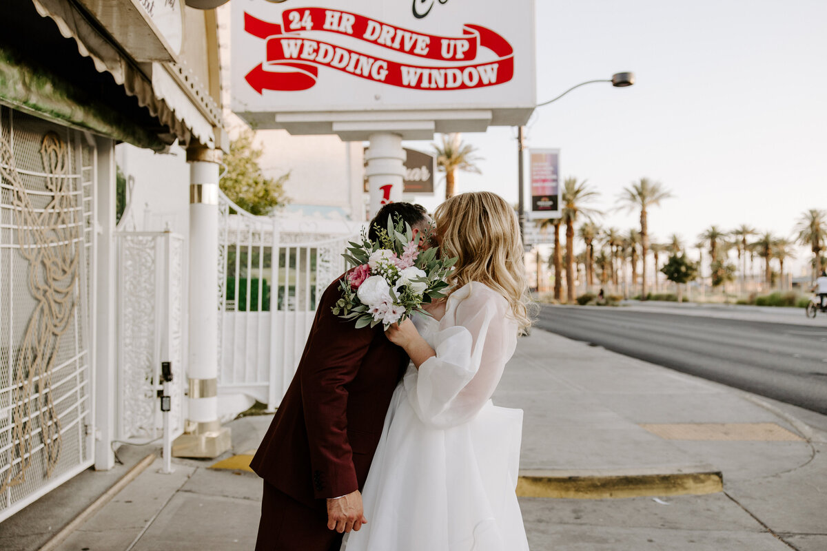 A couple kisses while the bride holds flowers at A Little White Chapel.