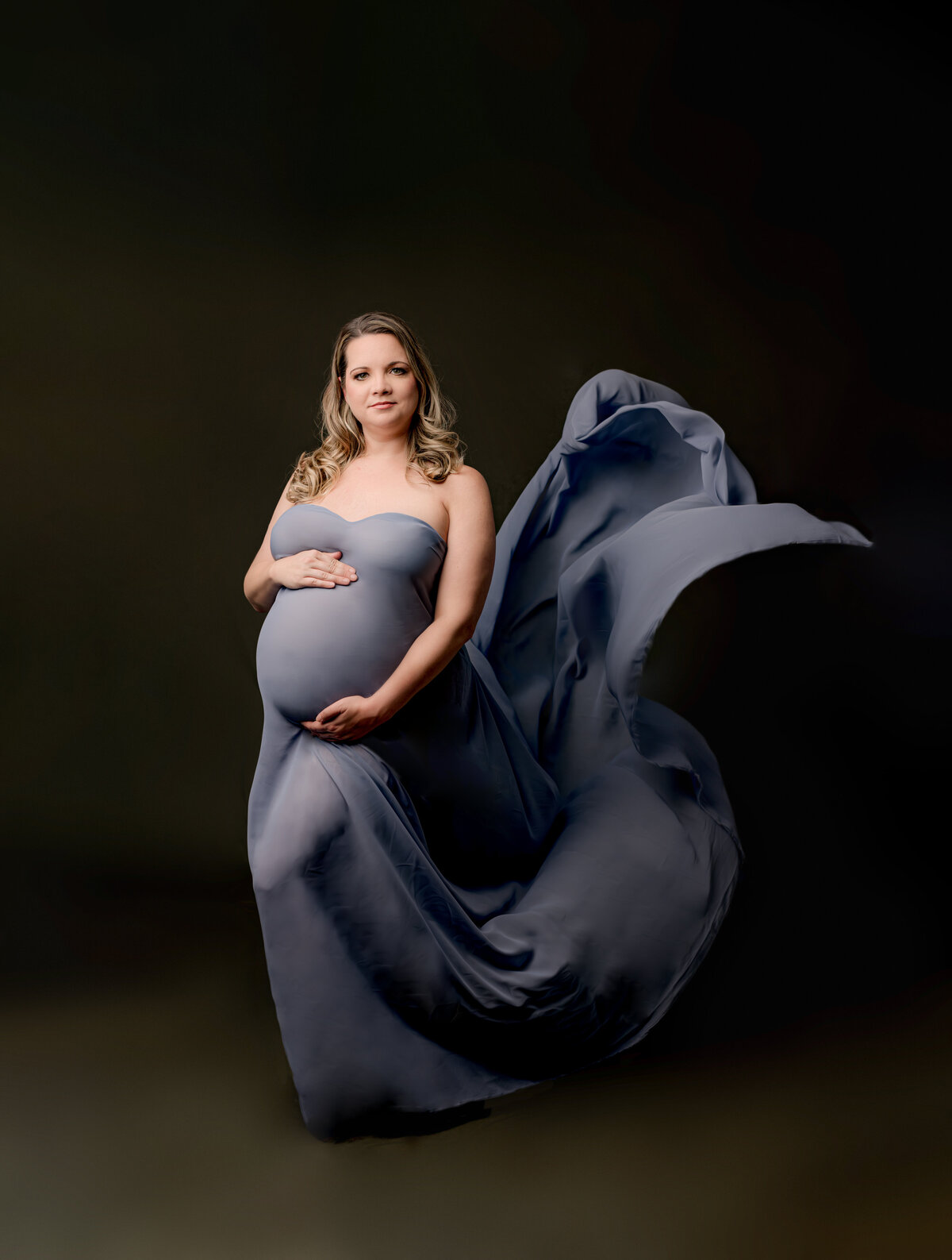 pregnant mother in blue chiffon dress on dark green backdrop