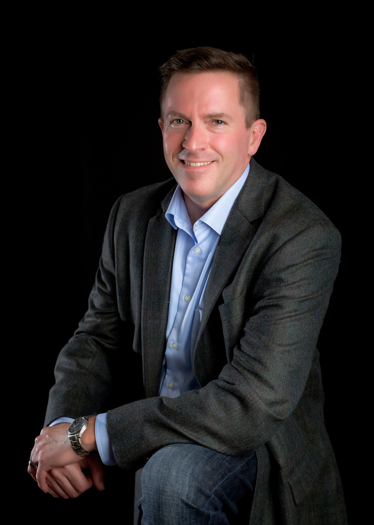 Male corporate headshot client wearing a suit seated with hands clasped