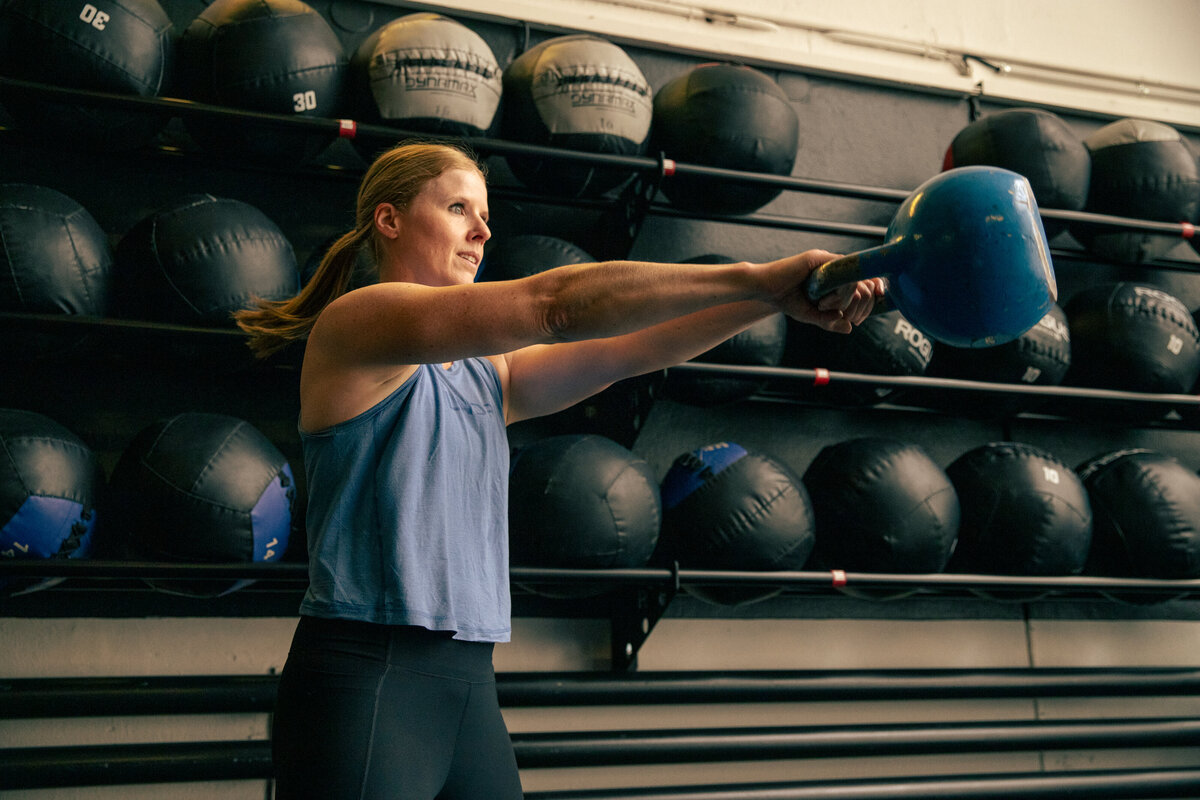 Sportliche Frau trainiert vor einer Wand mit Medizinbällen mit einem Kettlebell