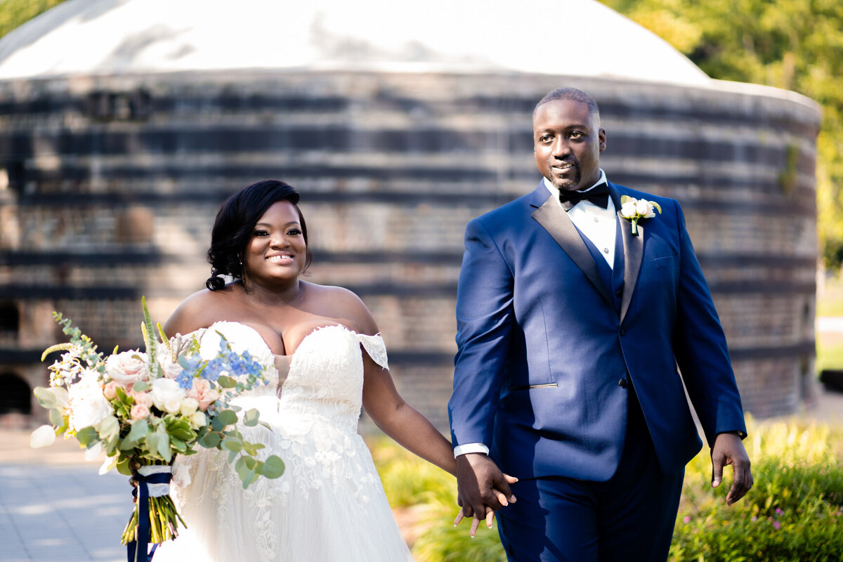 African American couple in wedding attire walk while holding hands.