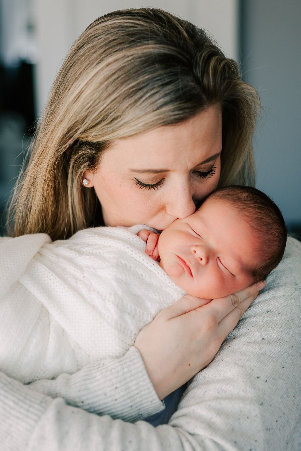 Mom holds and kisses her newborn baby during his newborn photoshoot.