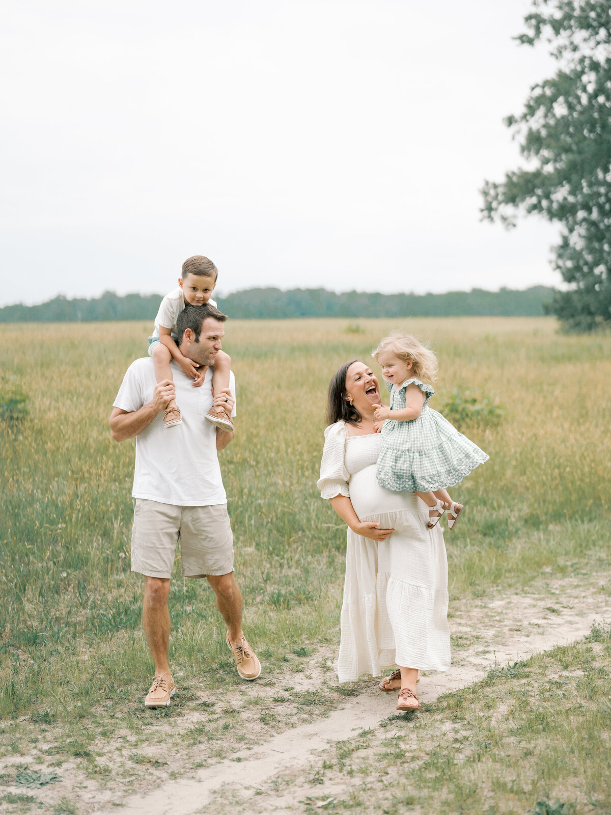 pregnant women and family laughing together in tall grass field