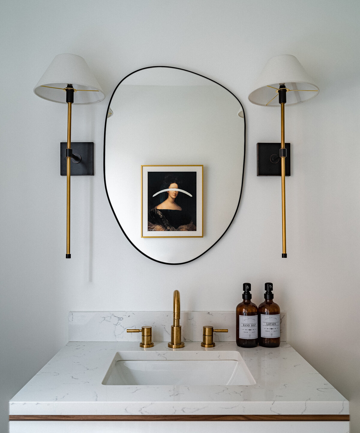 powder room with cvintage inspired artowrk, wall sconces and brass faucet