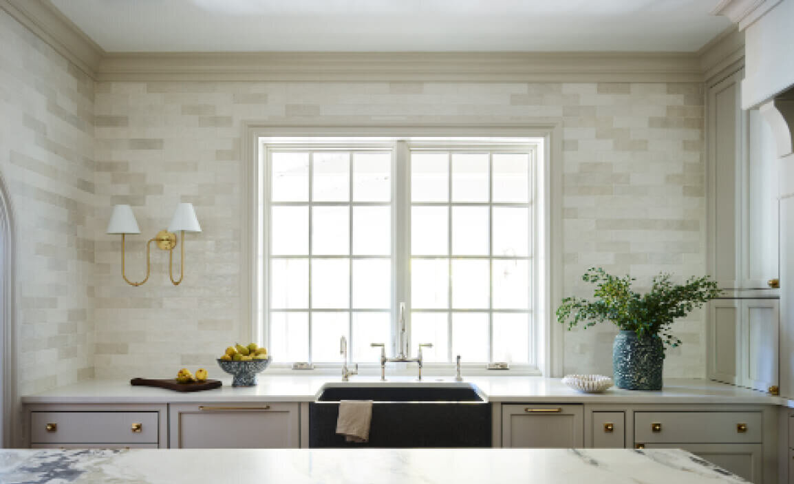 Boston area interior designers created custom white kitchen cabinets with artisan tile, a stone sink, and an Urban Electric light fixture for a timeless look.