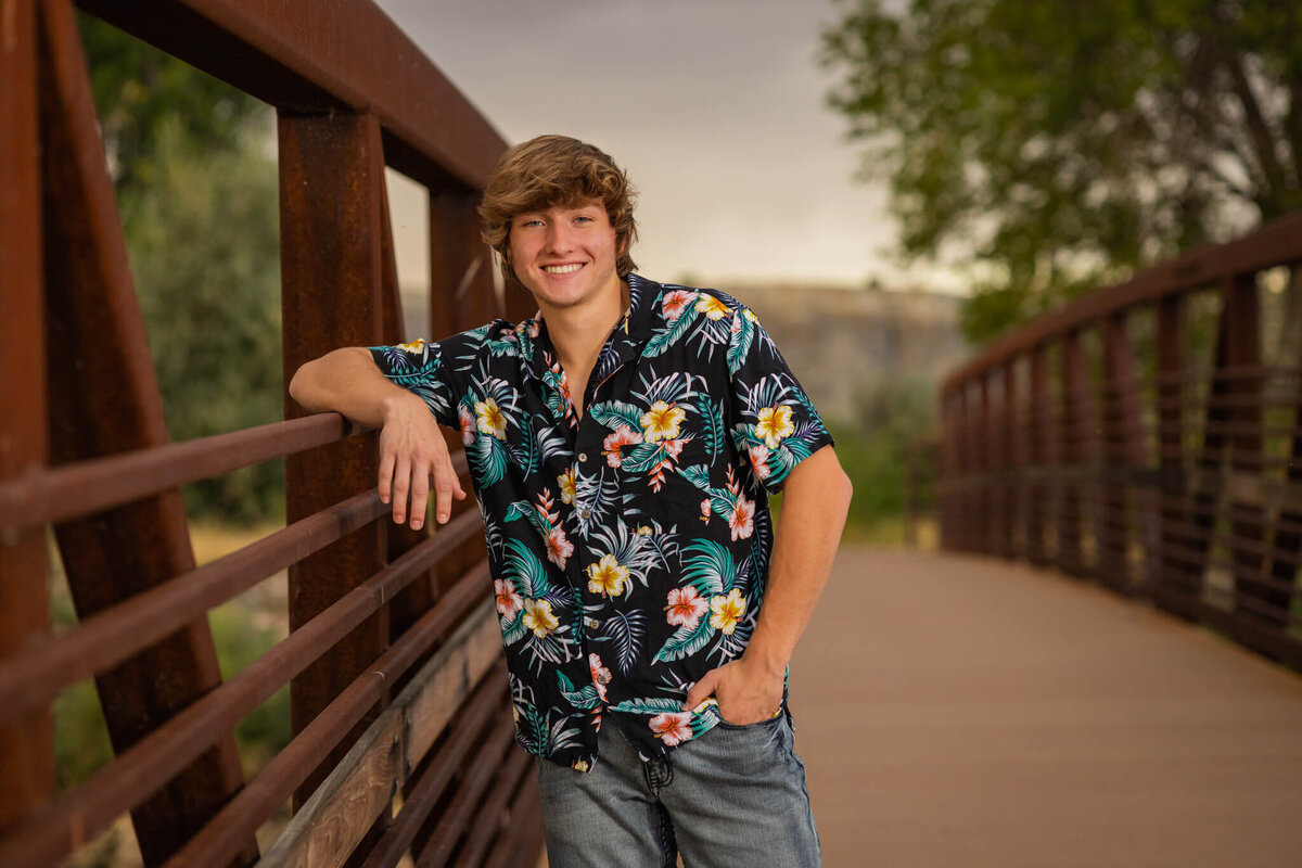 teenage boy wearing a hawaiin shirt leaning on a bridge
