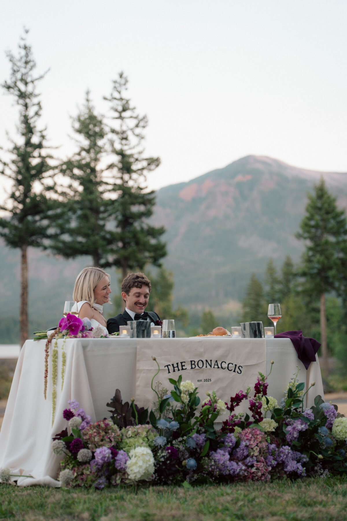Bride and groom seated at sweetheart table with floral décor and mountain view