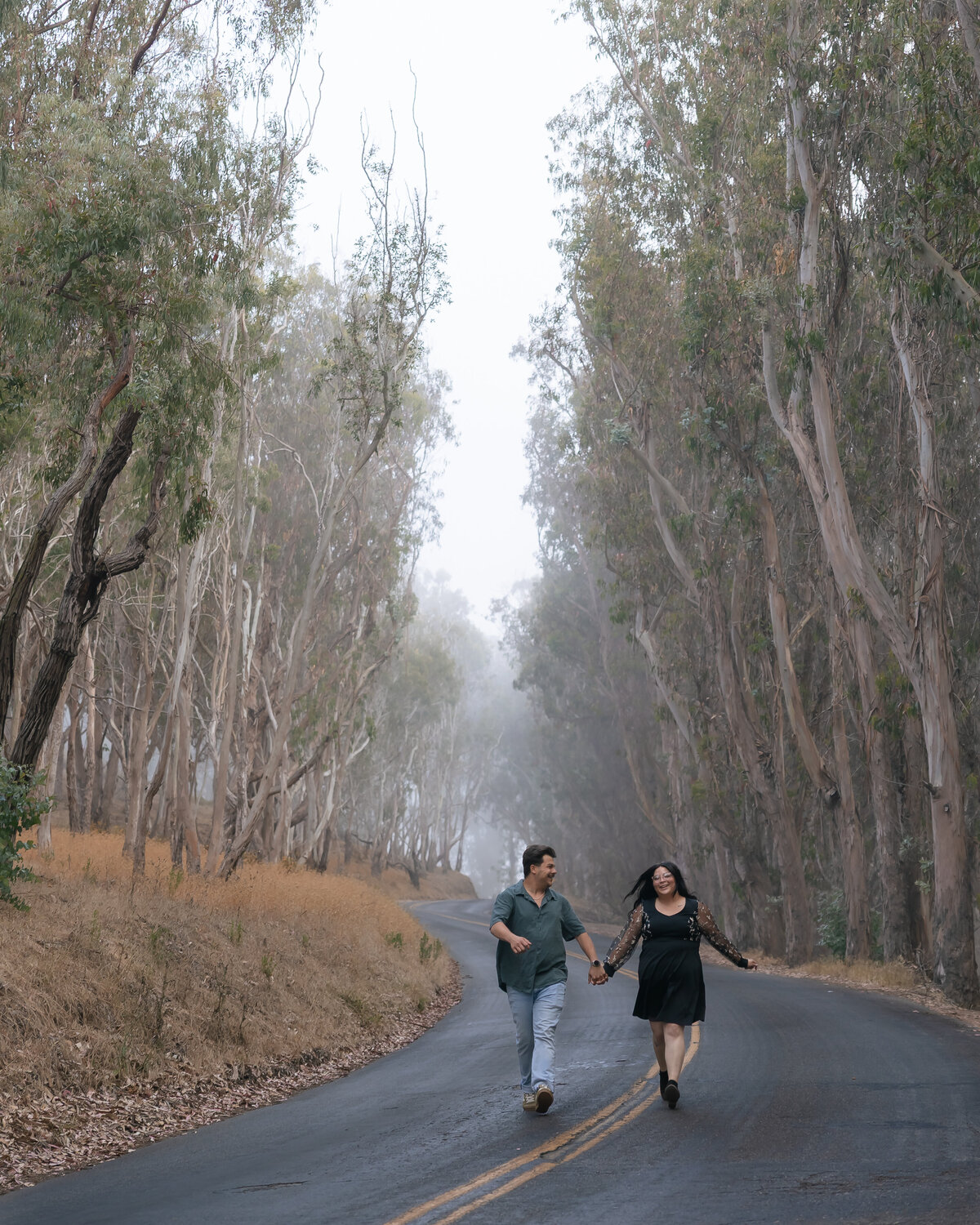 Candid Couples engagement photos at Montana De Oro on the Central Coast, with couple in road surrounded by trees and fog