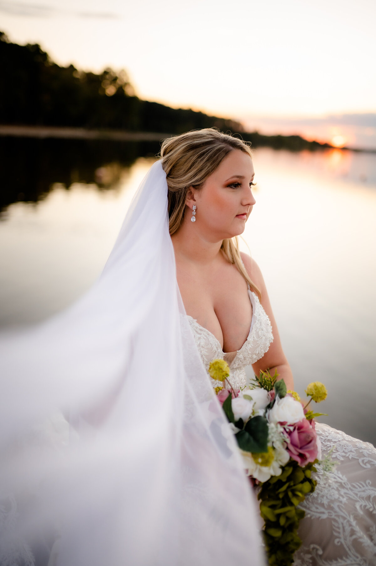 bride in a lace wedding dress holding her summer wedding bouquet and looking off in the distance as her wedding veil blows to the camera  captured by Best Little Rock wedding photographer