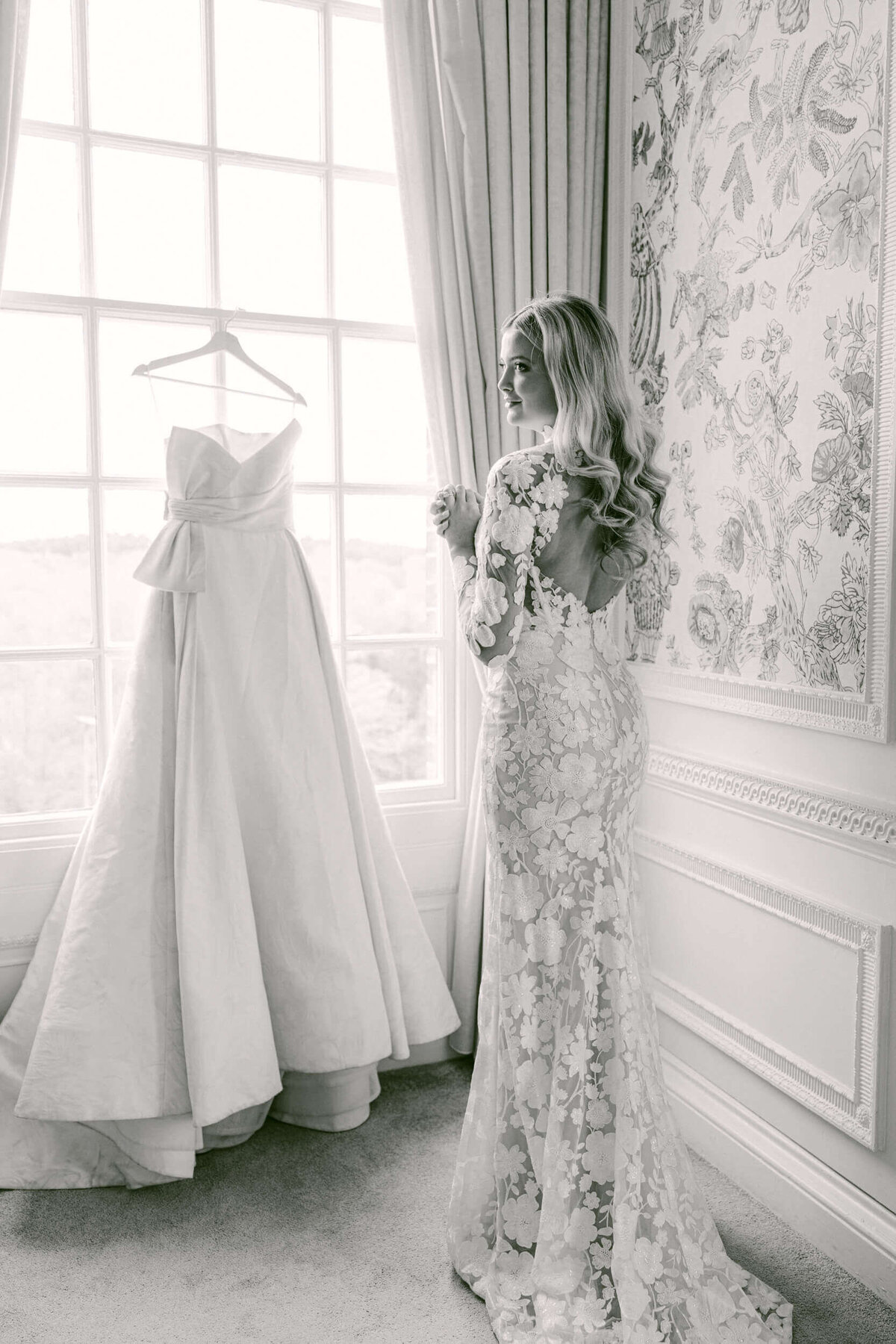 A black and white wedding photo of the bride looking at her wedding dress at Hedsor House in the UK