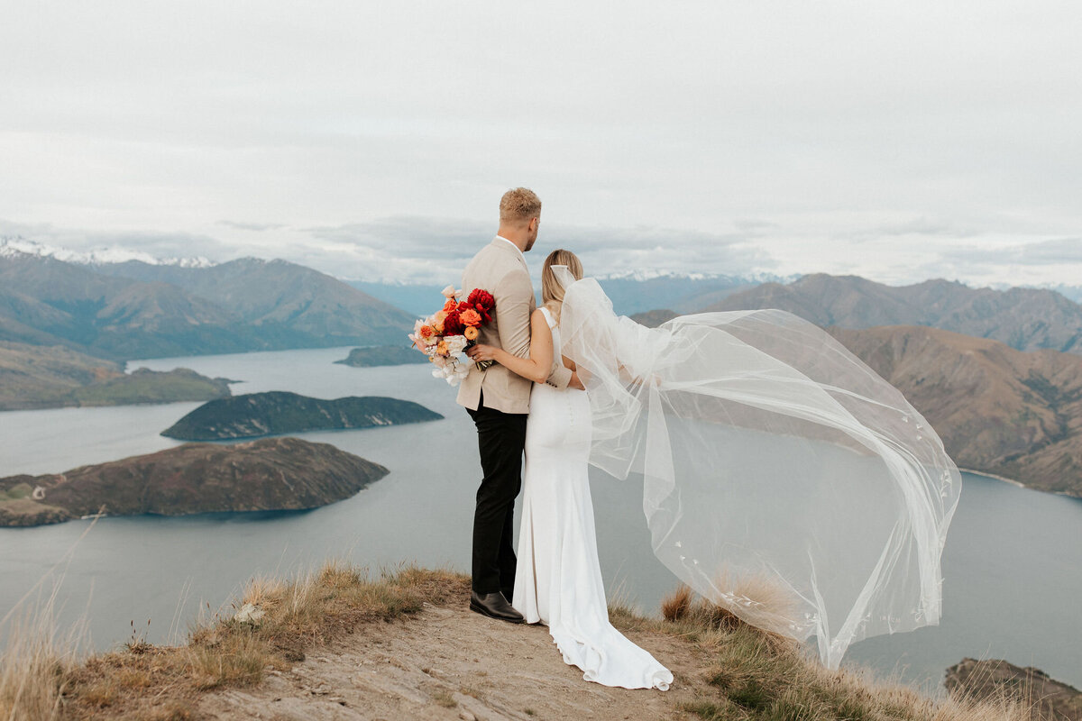 The Vase Floral Co - bride and groom on mountaintop in New Zealand, bride holding brightly coloured bouquet