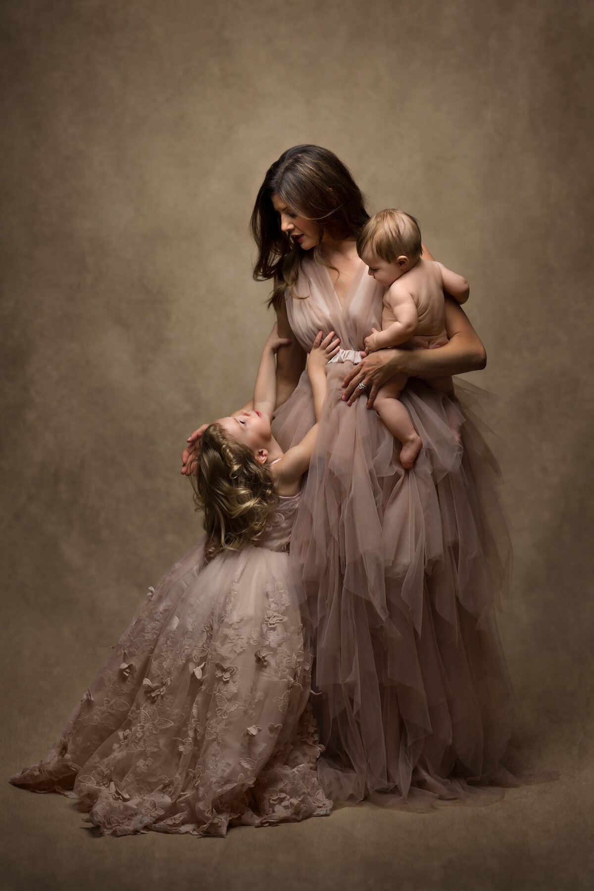 A mother lovingly holds her children, a newborn and toddler, in a warm and tender family moment. Captured by a Dallas family photographer.