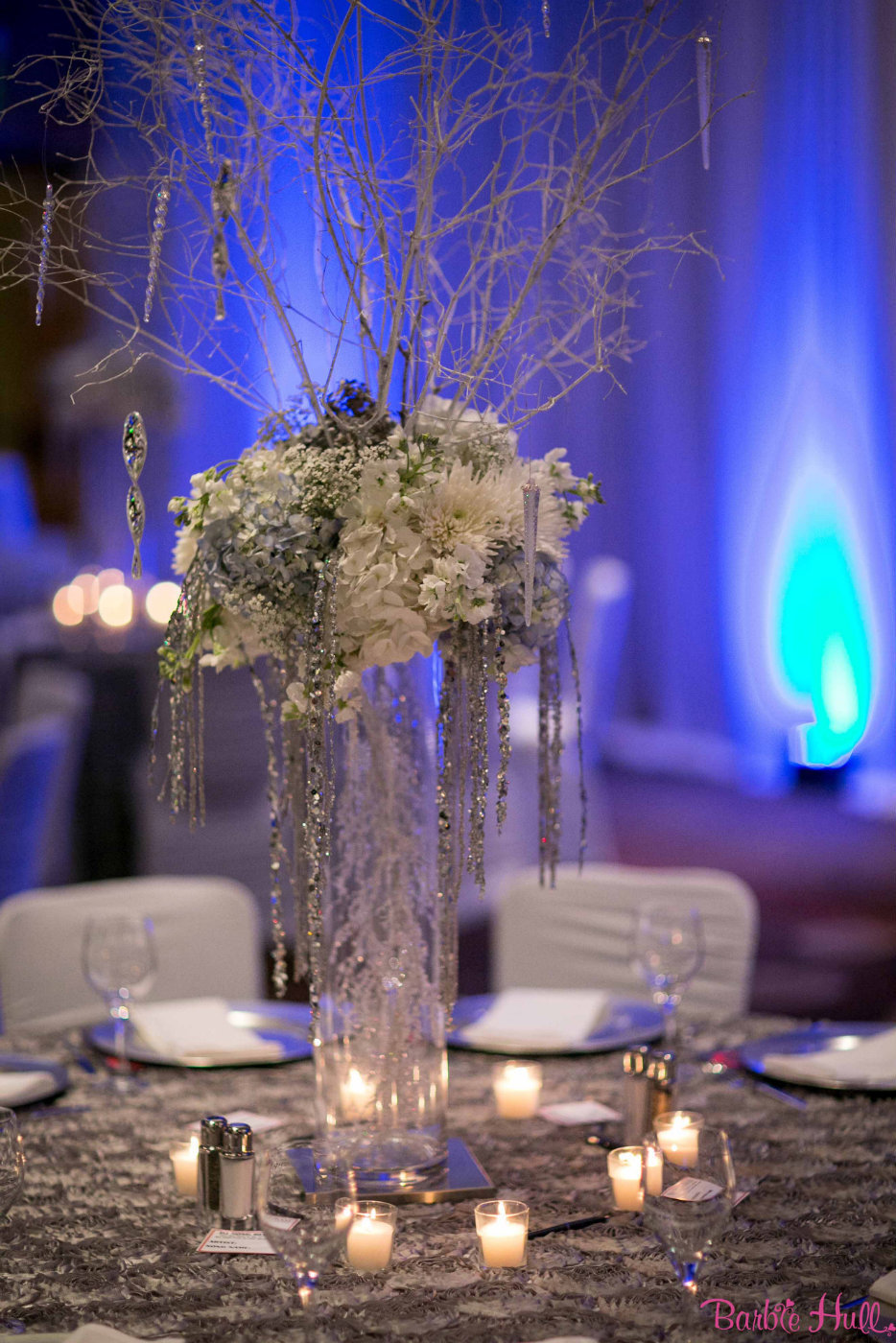 tall winter holiday party centerpiece with white hydrangea, white branches, crystal strands, blue uplighting for corporate party