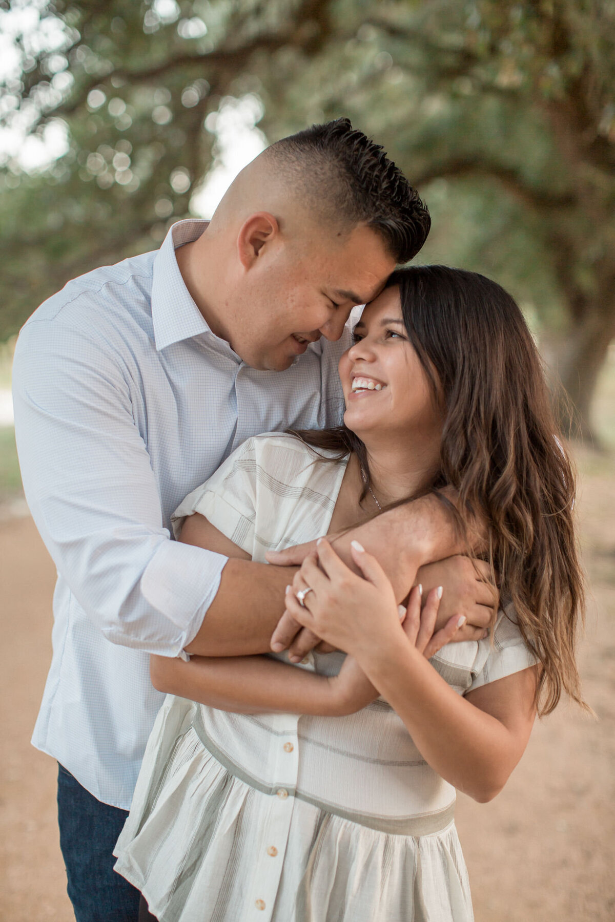 A man embraces his fiancee from behind, pulling her into a warm embrace