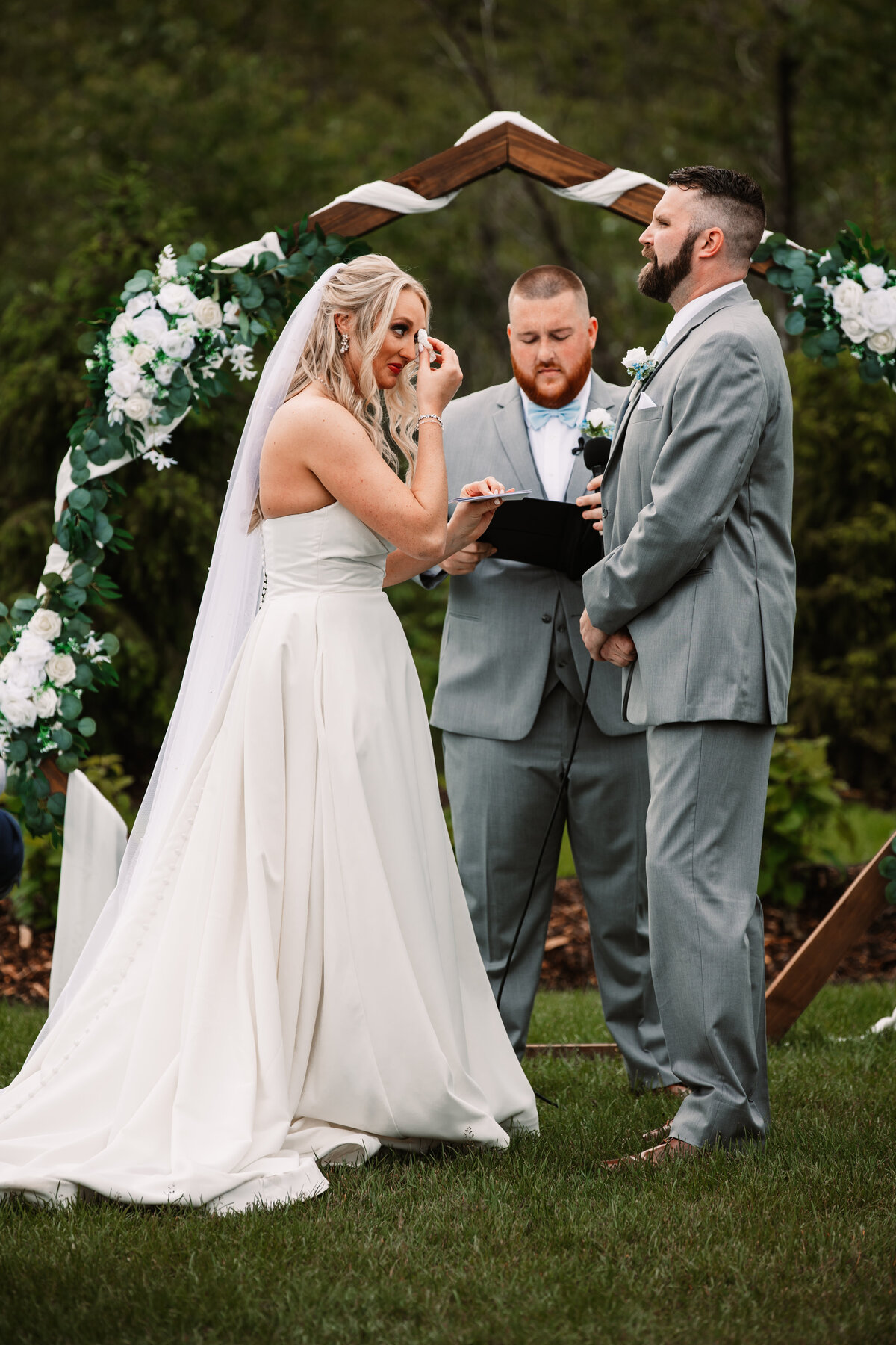 A bride wipes away tears while standing at the altar with her groom