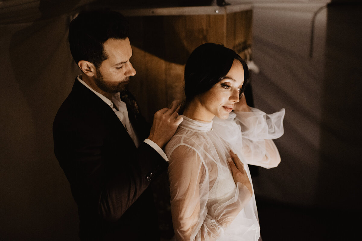 Utah elopement photographer captures groom buttoning bride's dress before wedding