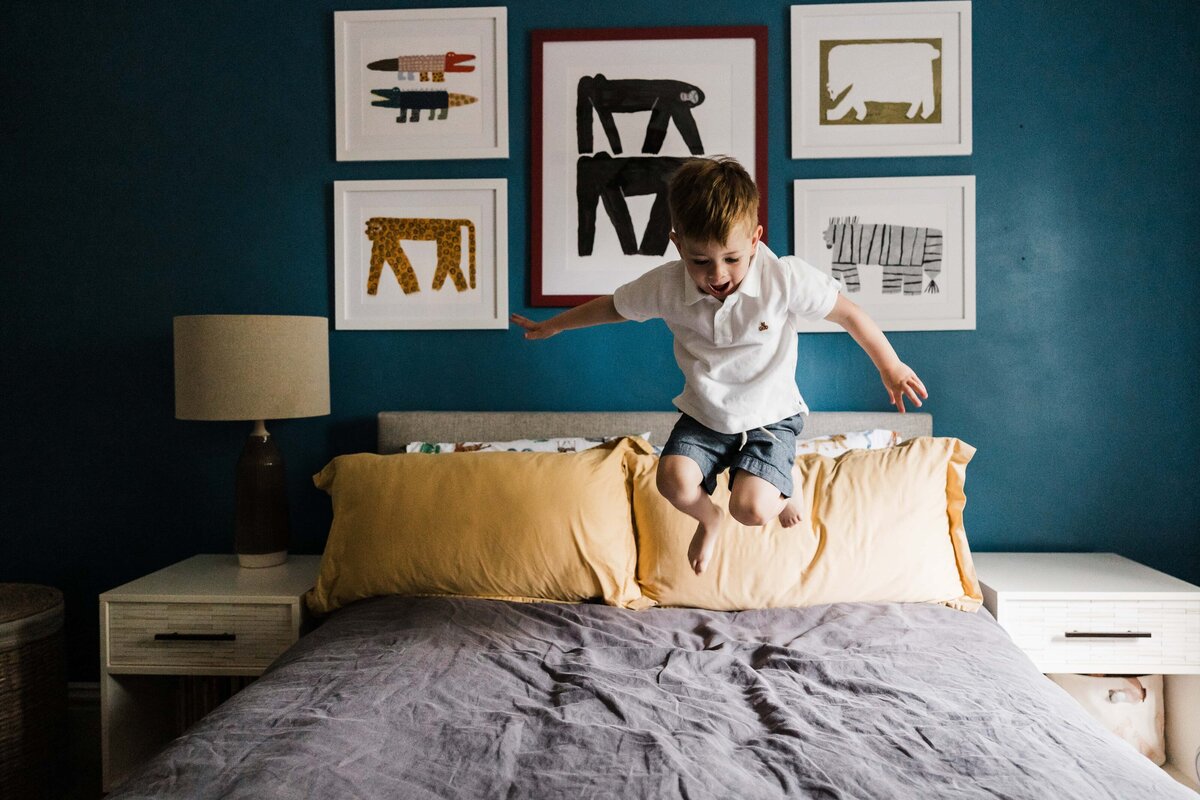 A child joyfully jumping on a bed in a room with animal-themed artwork on the wall, captured by a talented Pittsburgh family photographer.
