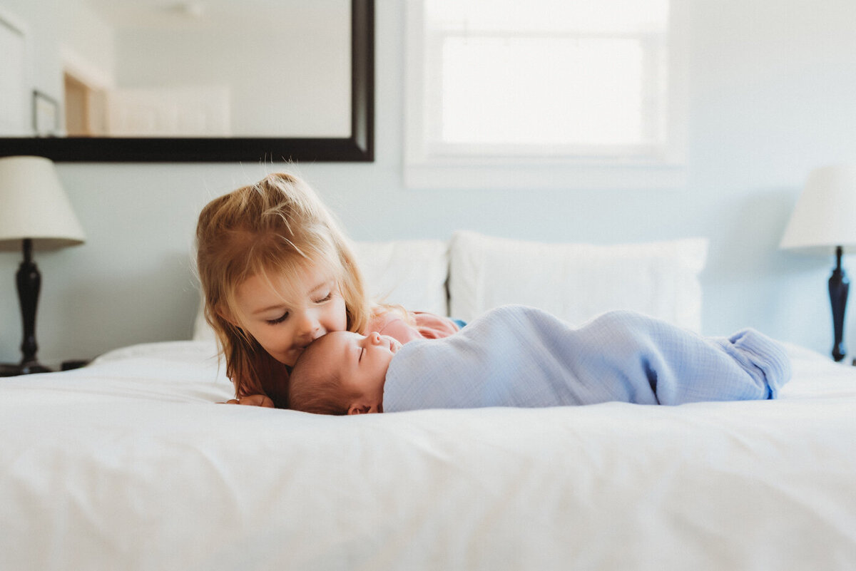 New Big sister kisses baby on bed