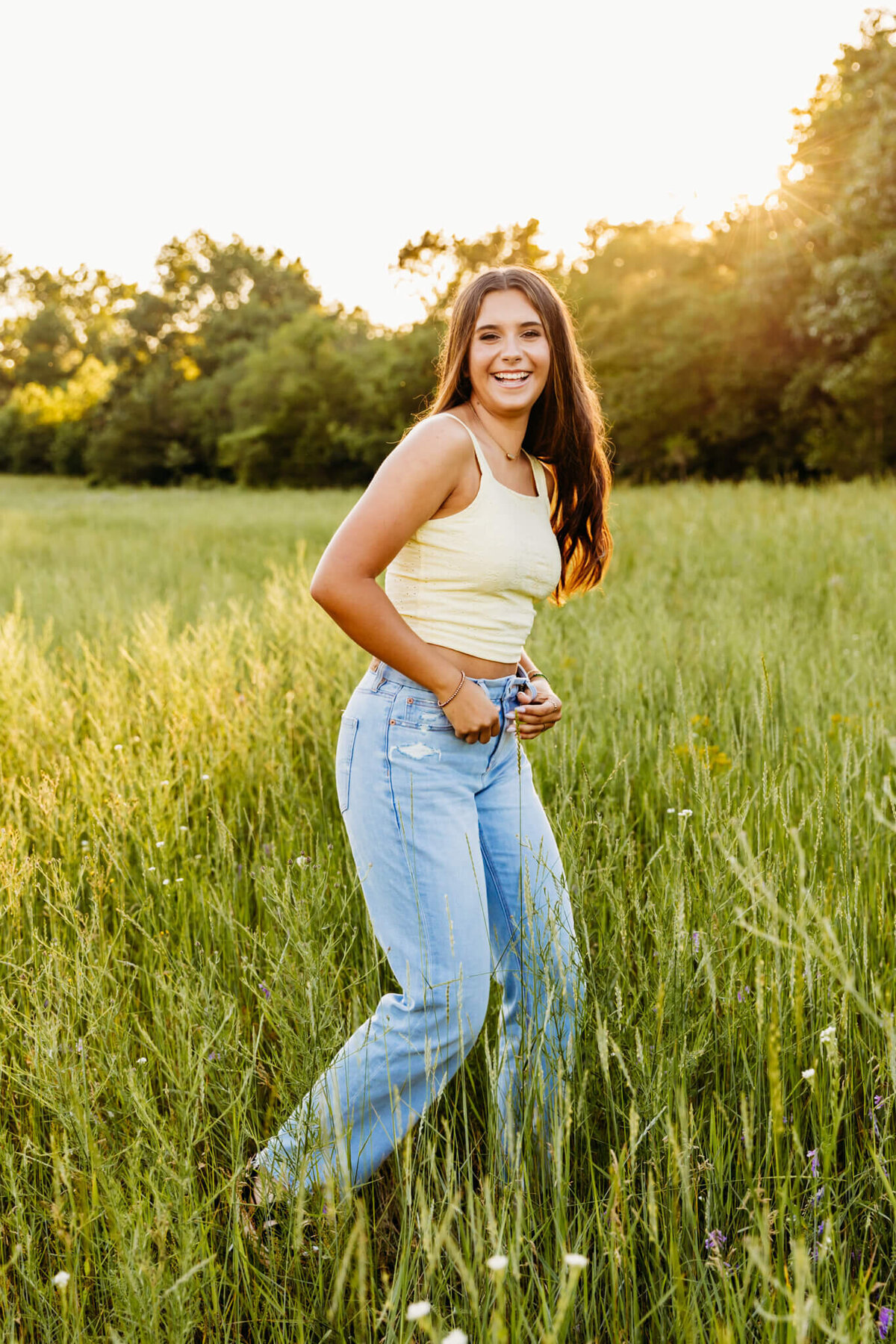 teenage girl resting her thumbs in her belt loops as she moves forward and laughs captured by Oshkosh senior photographer Ashley Kalbus