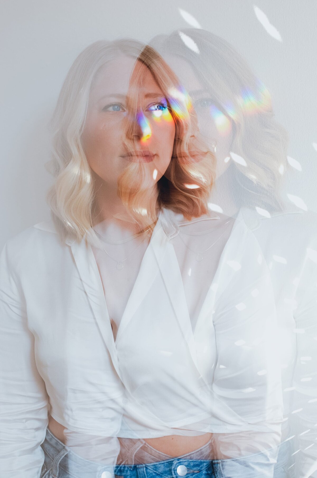 Double exposure of woman with blonde, wavy hair and silk, white top with rainbow and disco ball reflections on her face.