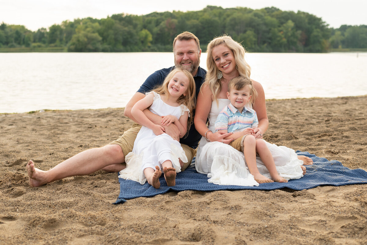 Family snuggling together on a blanket at the beach, smiling for a portrait. 