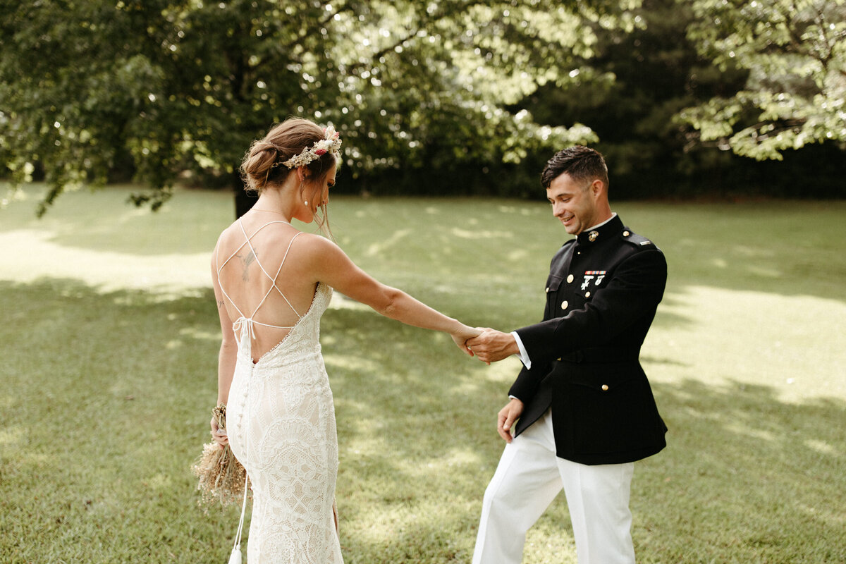 Bride in backless intricate lace dress dancing with military groom in uniform