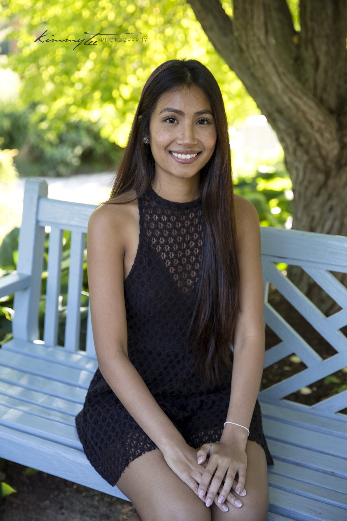 Smiling girl in black dress sitting on a blue bench