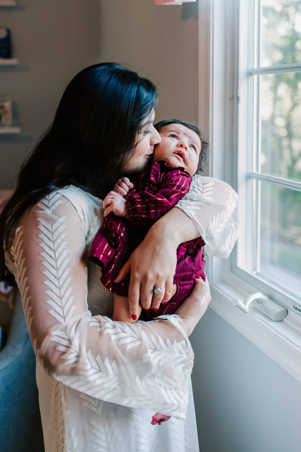 mom kissing baby girl's cheek next to a window in their Reston VA home