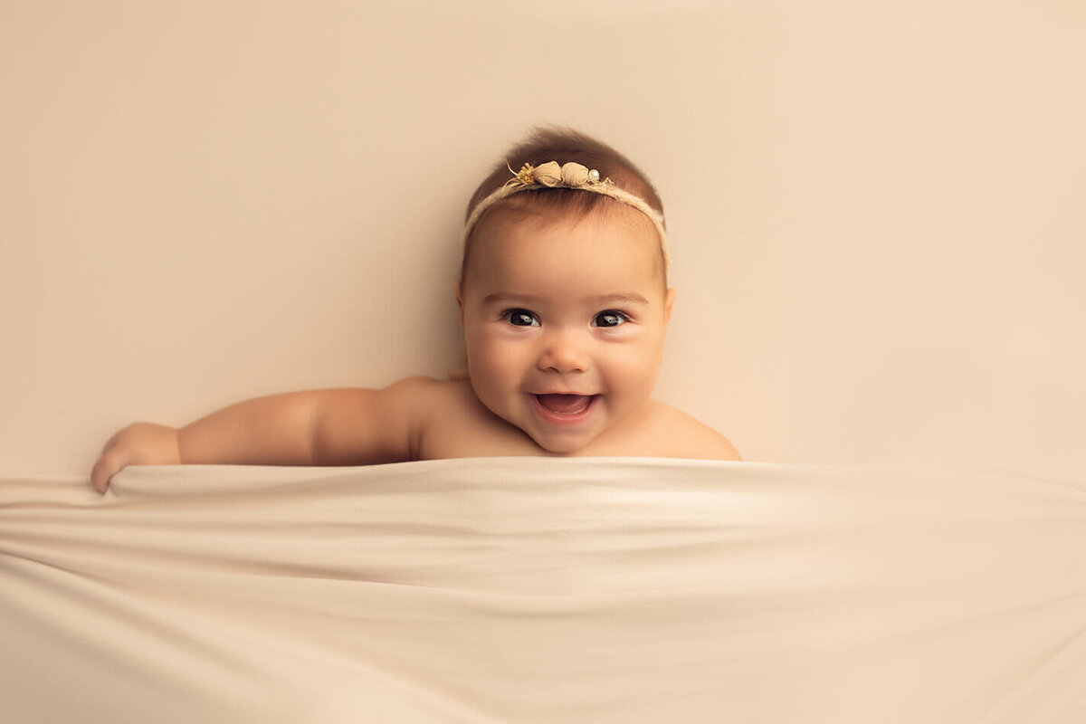 a six month old girl tucked into some cream fabric laughing at the camera