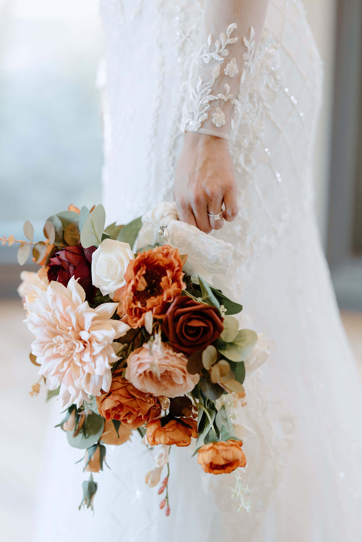 bride holding fall colored  bouquet in hand against vintage lace wedding gown