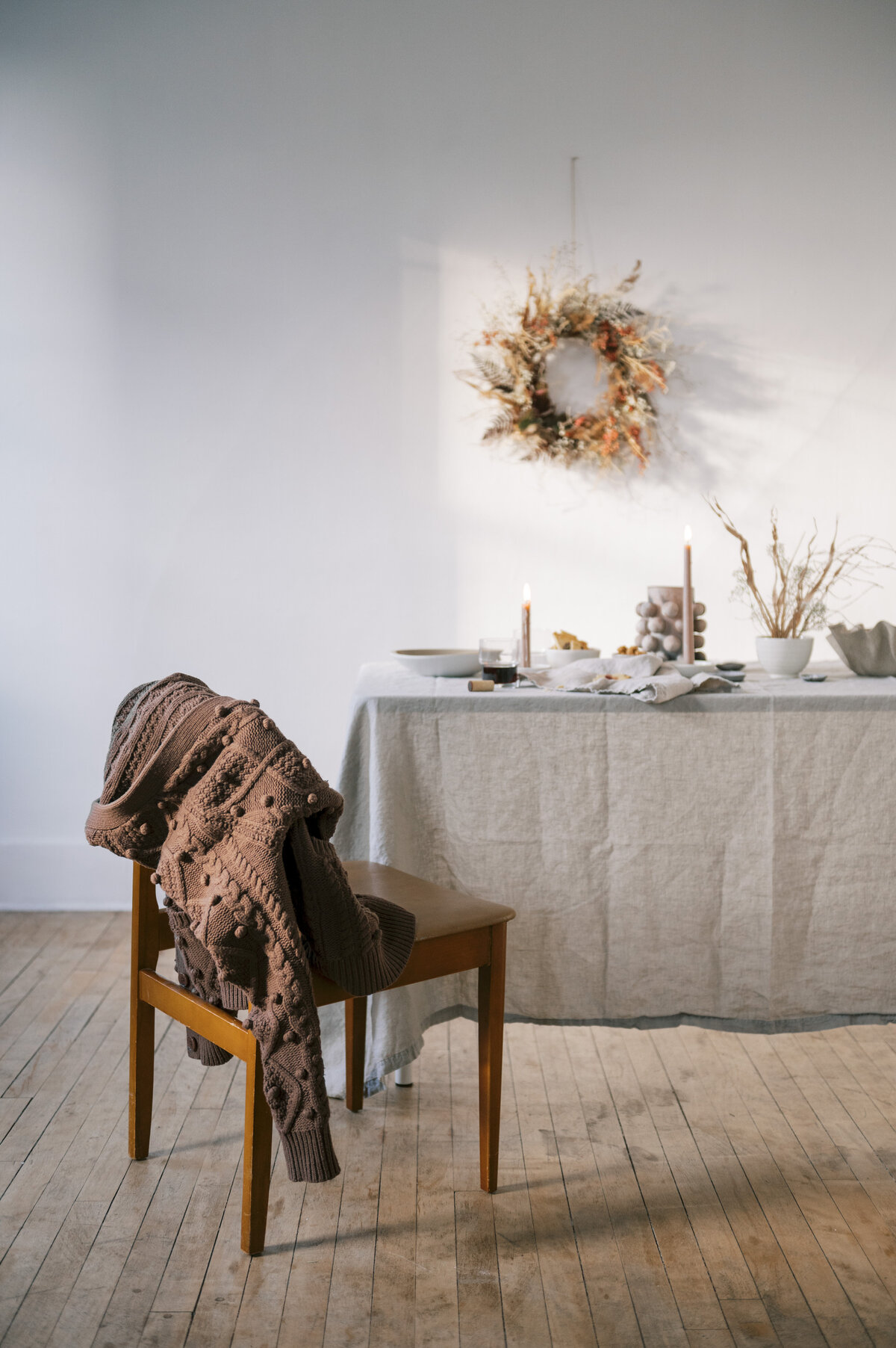 Grey minimalist Scandi tablescape with wine and bread on table next to wooden chair with brown sweater