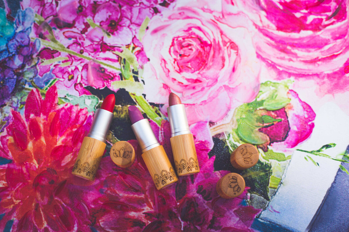 A collection of red, pink, and brown lipstick by Elate Cosmetics on a floral background.