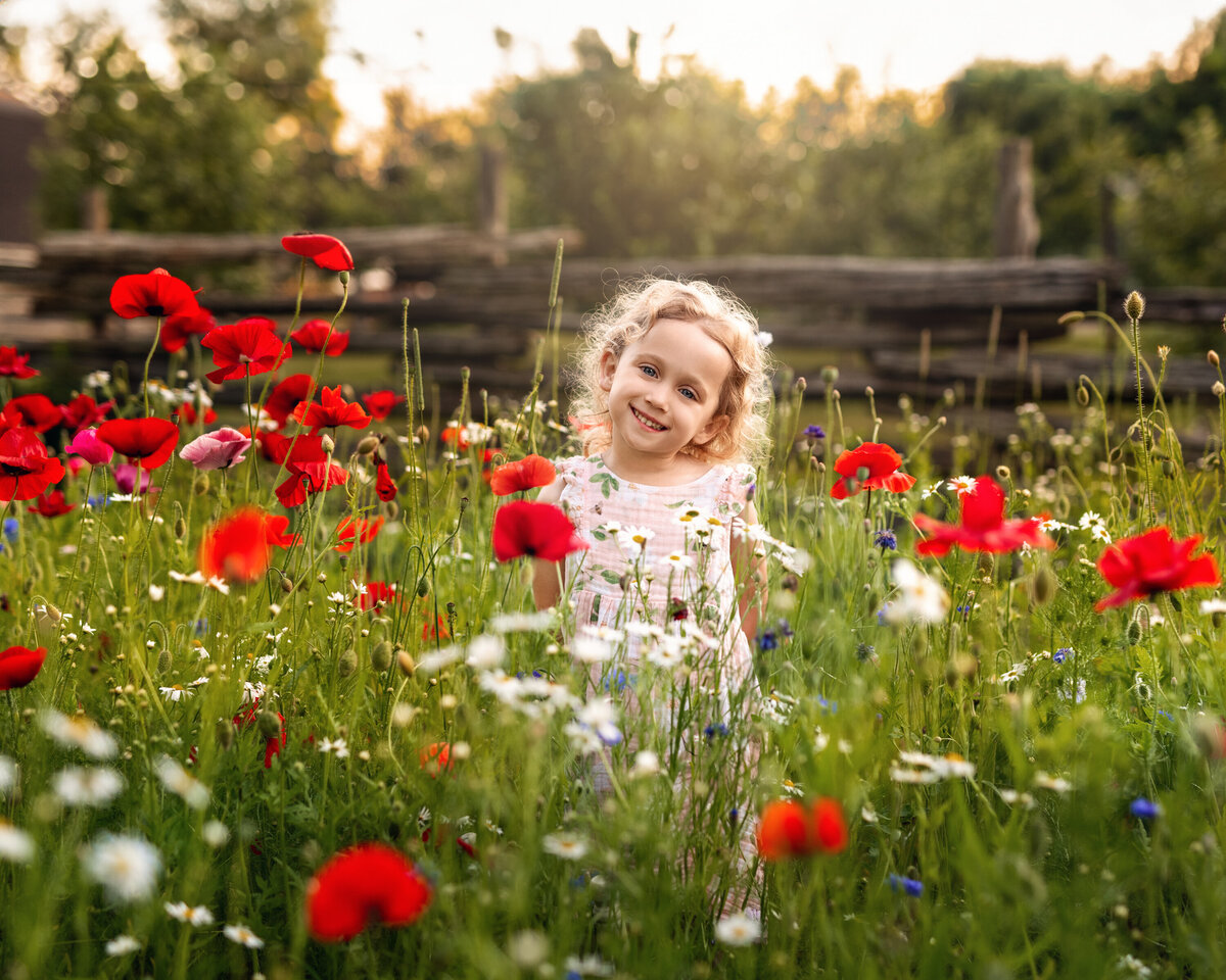 Outdoor milestone photo of a smiling girl in a wildflower field—capturing childhood wonder in golden summer light.