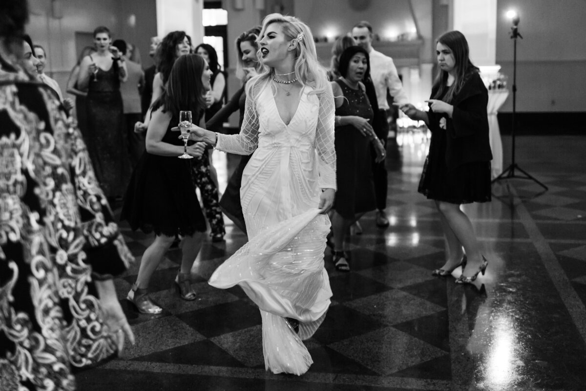 Black & white candid of a bride dancing with champagne in her hand captured by Fort Worth wedding photographer, Megan Christine Studio
