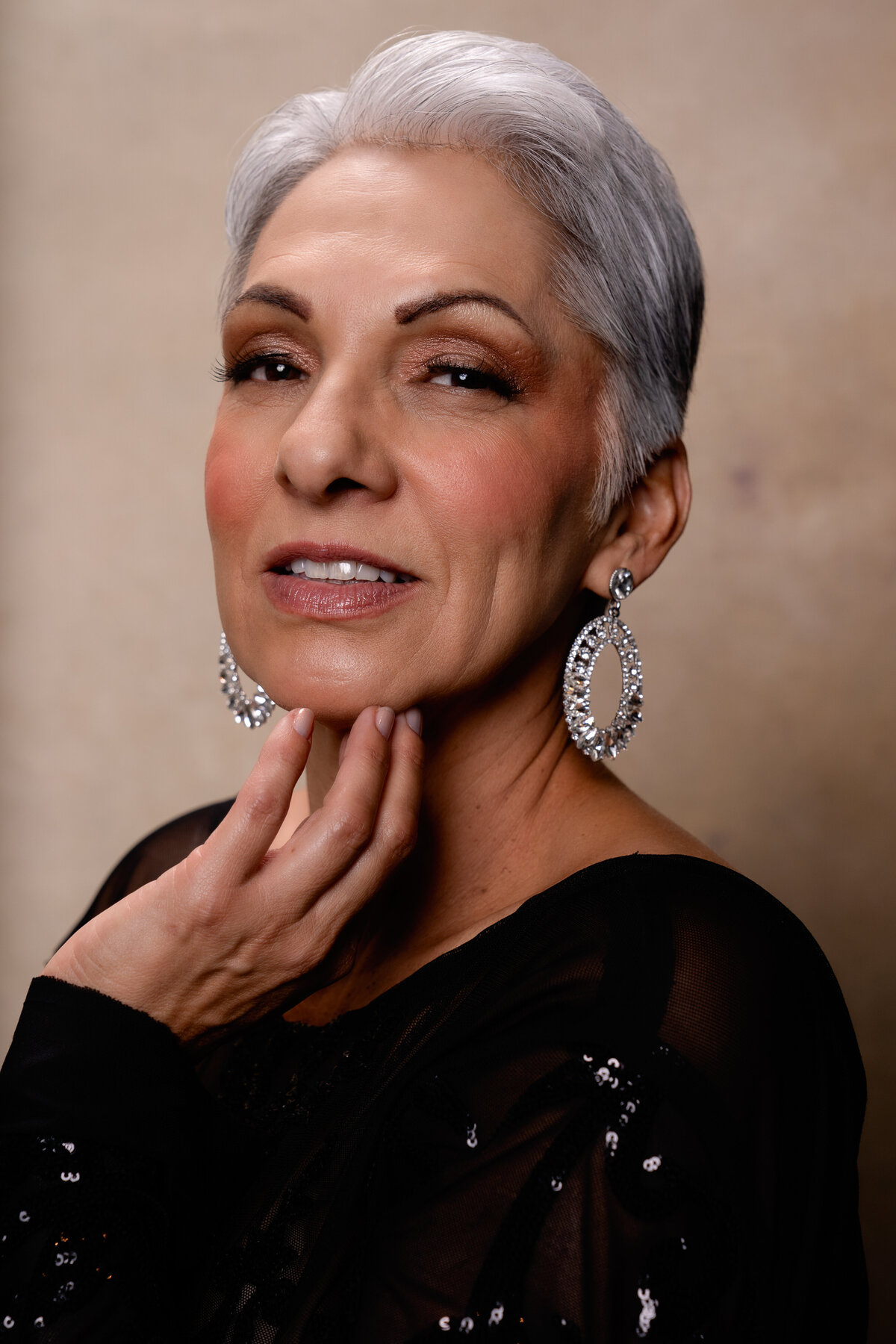 Middle Aged woman with short gray hair standing in black dress on a beige backdrop.