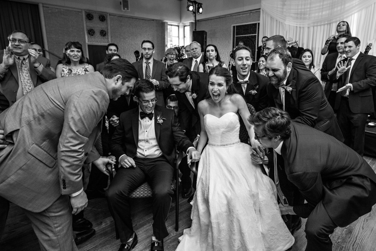 A jewish wedding couple are lifted by wedding guests for The Hora.