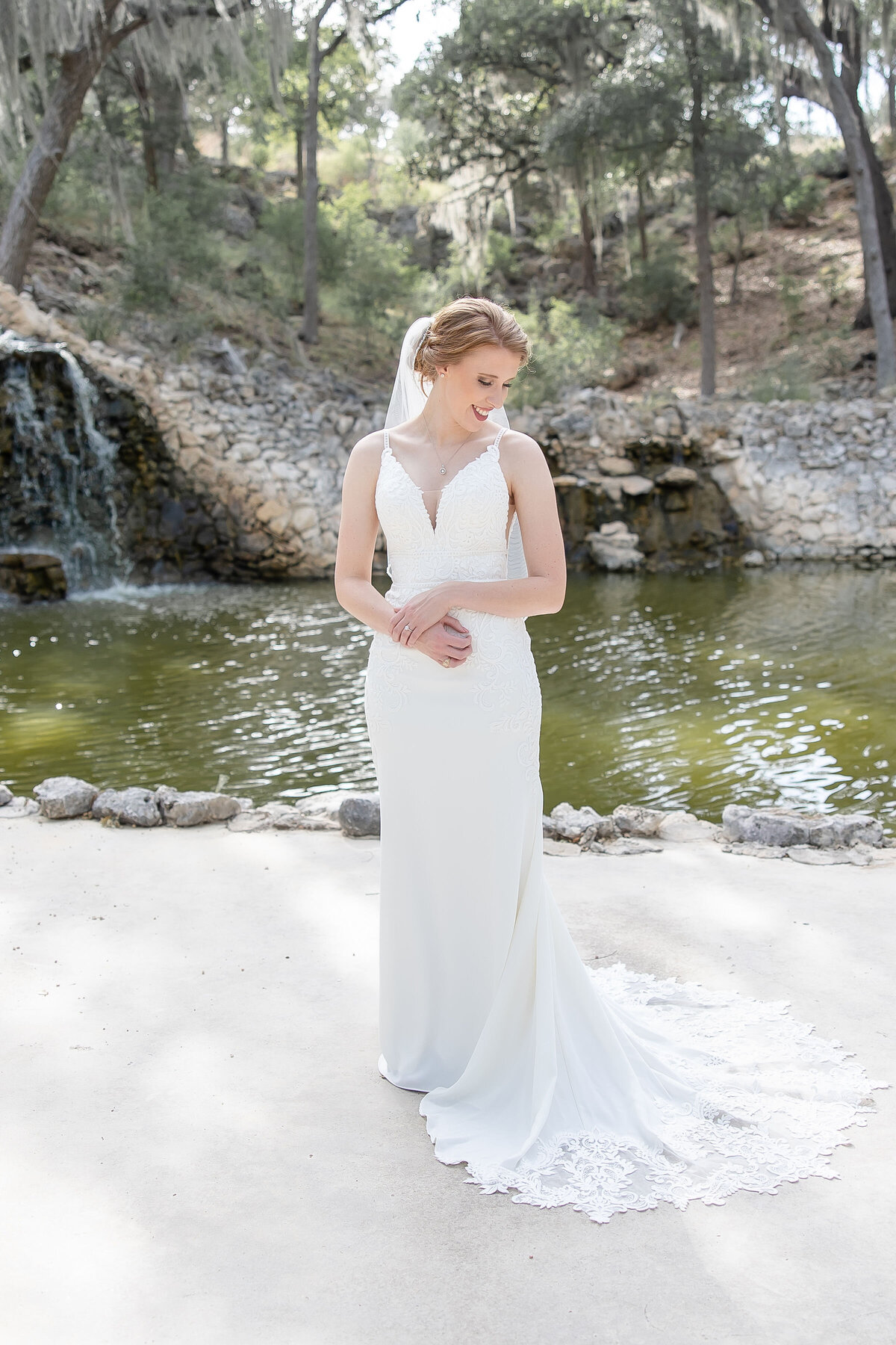 bride holds wrist and smiles with waterfall behind at Hayes Hollow at Hidden Falls in Spring Branch Texas