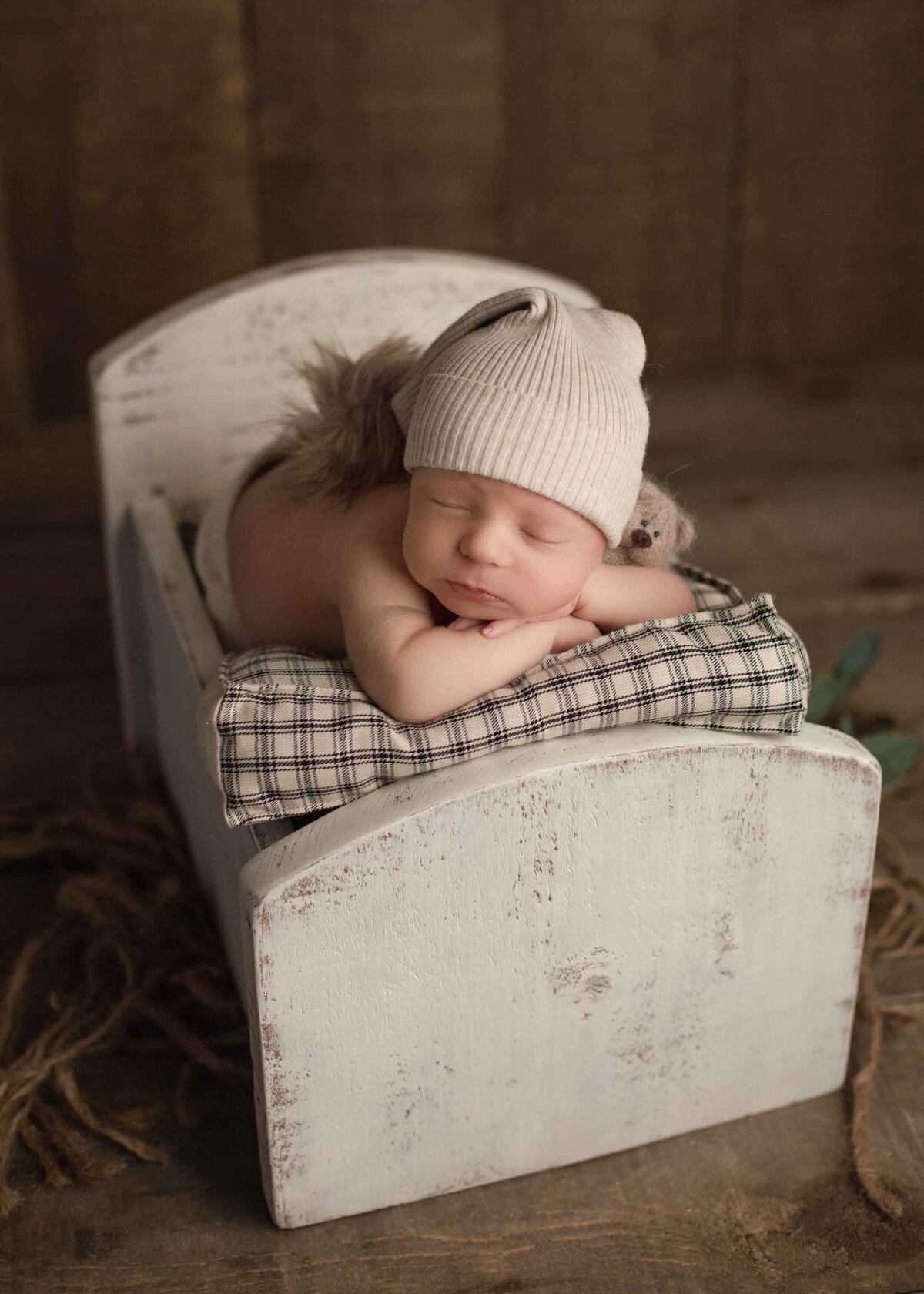 Newborn boy in a mini bed with a fluffy hat on