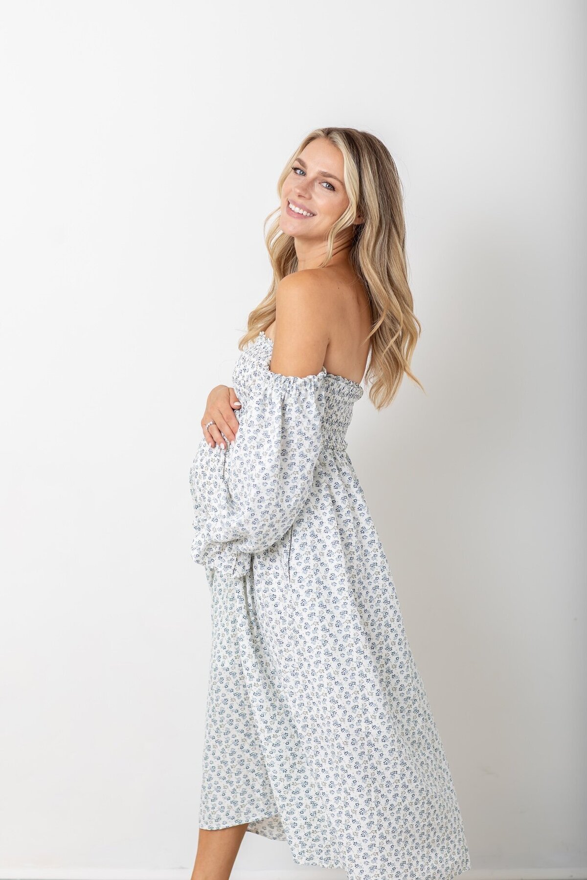 Expectant mother in a white and blue dress posing outdoors, cradling her belly—photographed by Philadelphia maternity photographers.