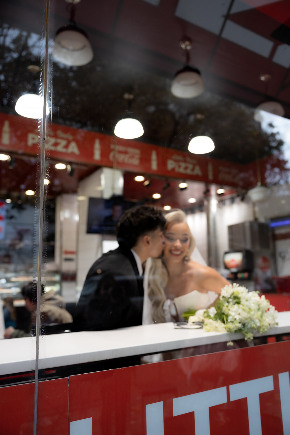 Urban NYC elopement: The couple sits at a pizza shop table with pizza slices and drinks.