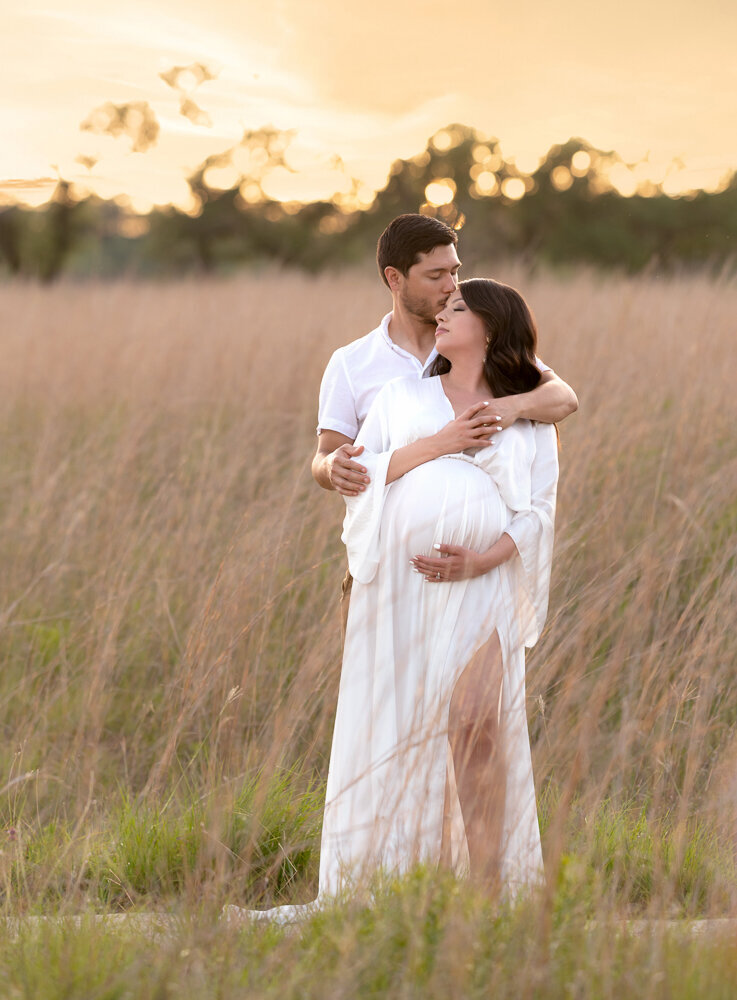 Sweet and warm maternity portrait of a couple in a Westlake field at sunset, with soft light and flowing dress.