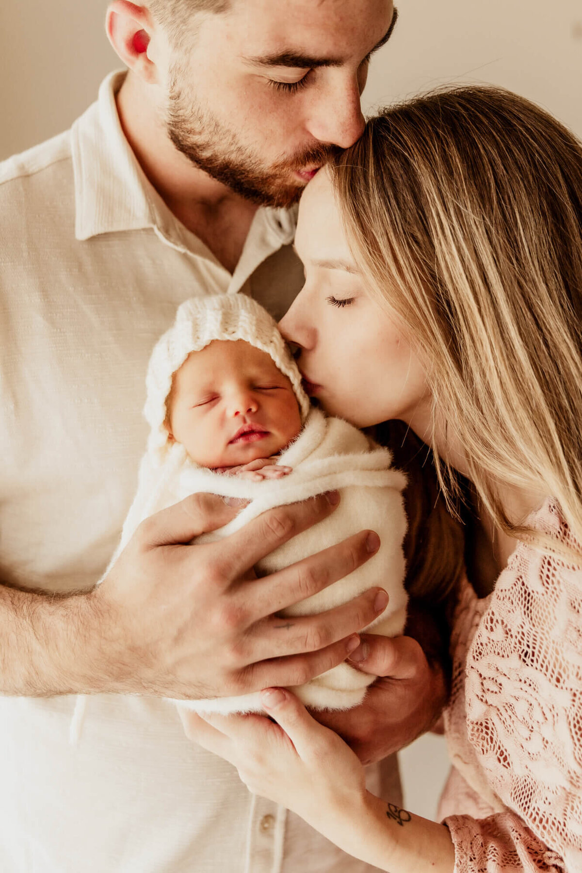 Mother kisses her baby girl's head who is being held by the baby's father.