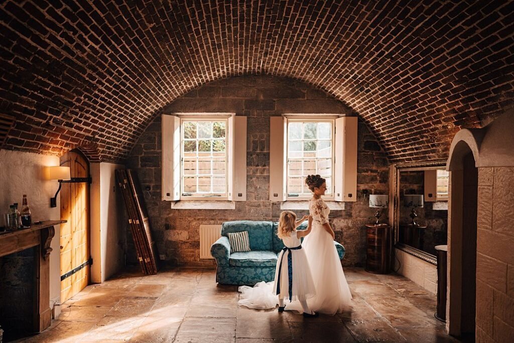 A bride and her flower girl in a brick walled room