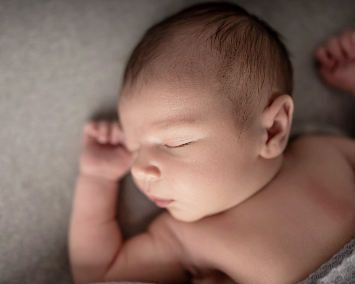 A newborn sleeps on its back with arms up