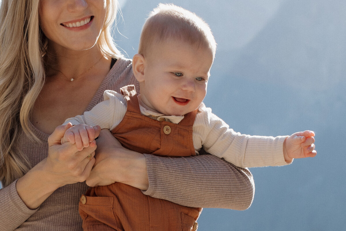 A mother holding her baby’s hand, framed by stunning mountain scenery, captured with an editorial wedding photography touch.