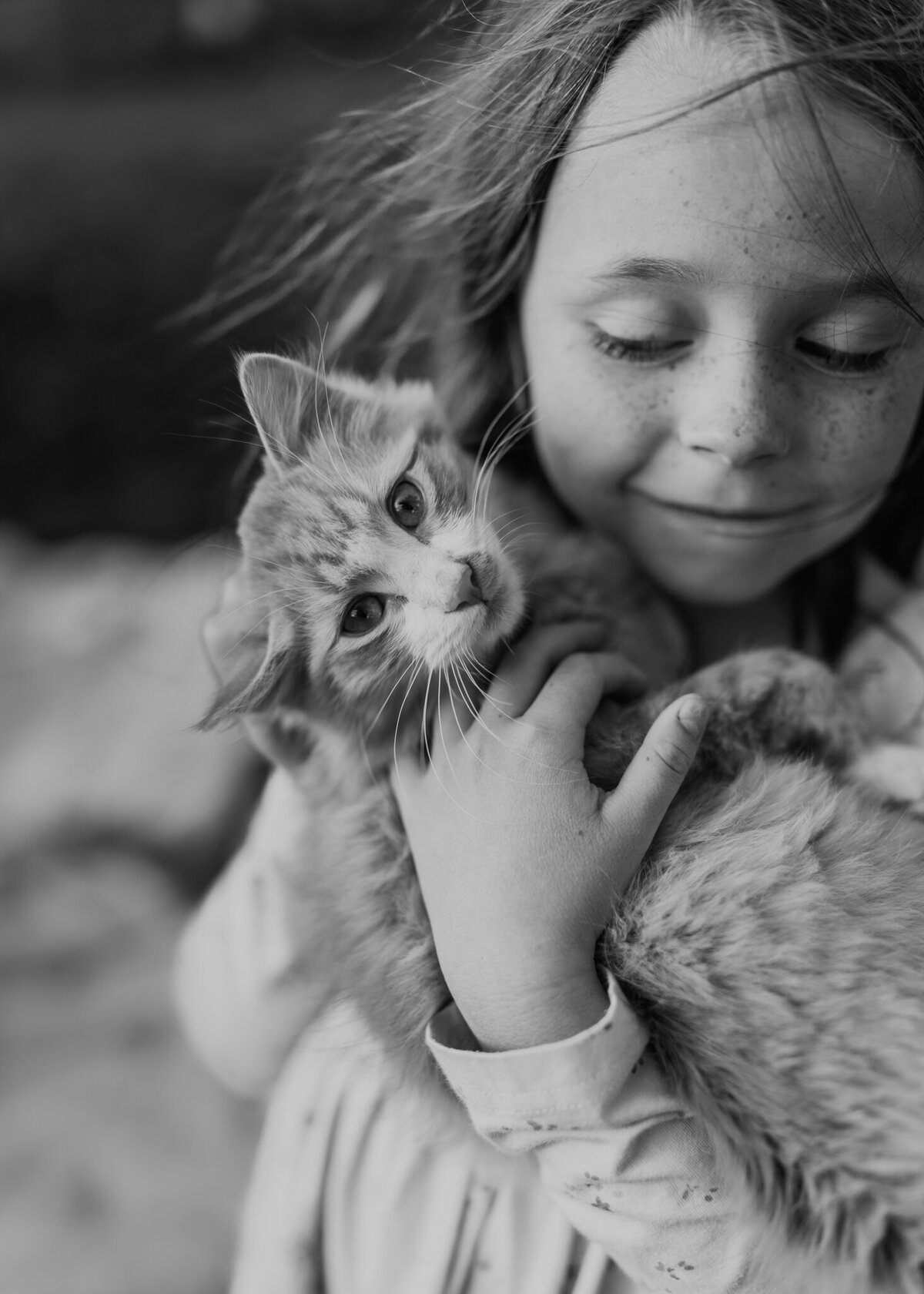 A black and white fine art portrait of a young girl lovingly holding her favorite kitten on her family's farm.