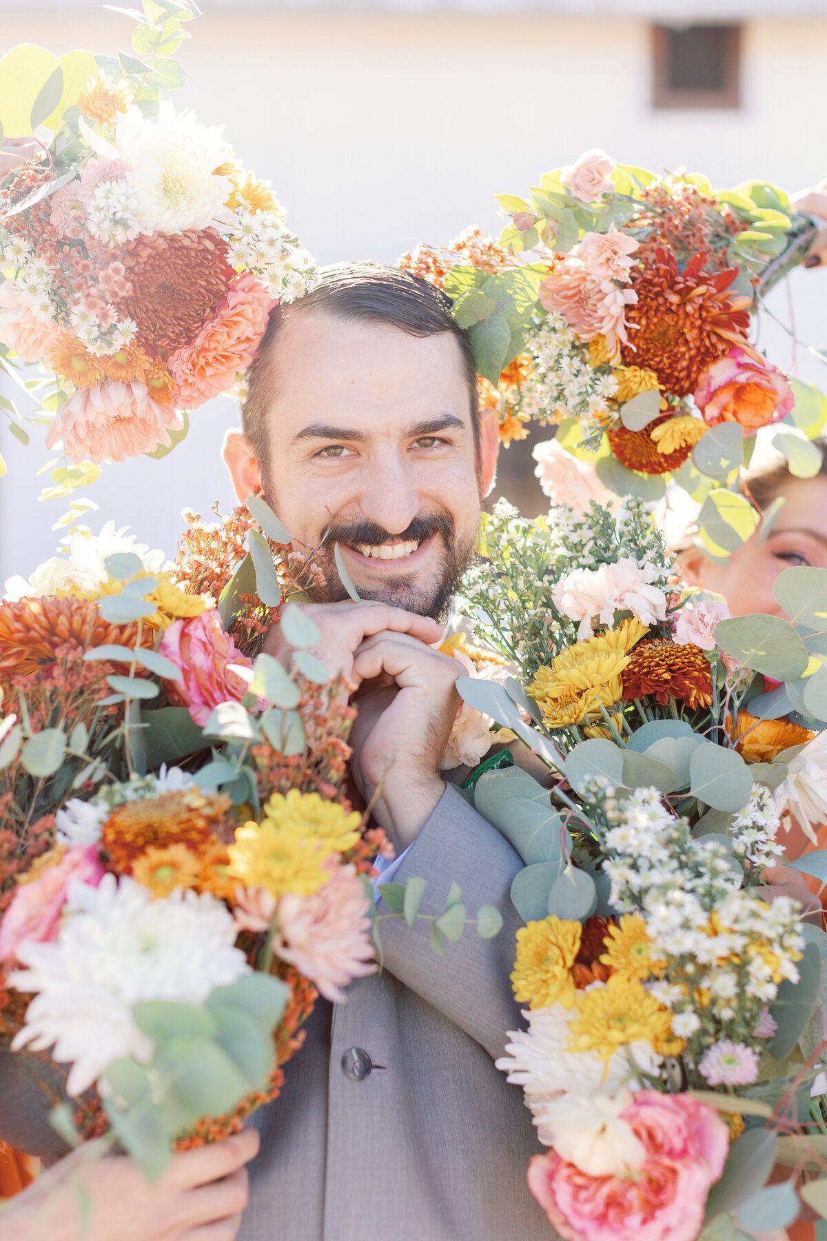 Groom playfully posing with colorful bridesmaids’ bouquets during fun wedding party portraits.