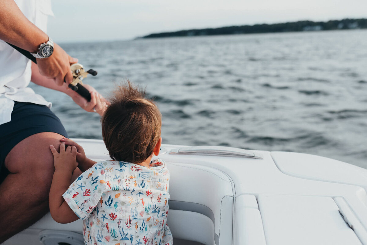 A young boy holds on to his father's leg on their family boat at sunset