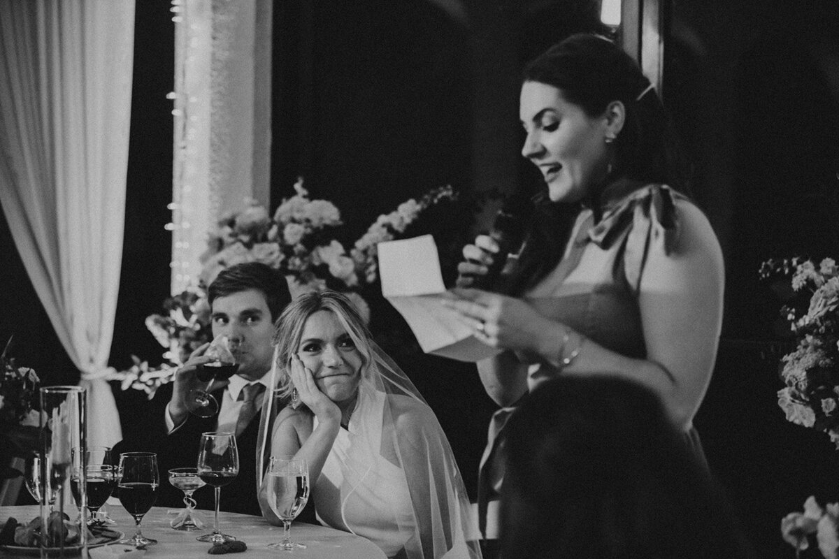 maid of honor gives speech while bride looks at her fondly