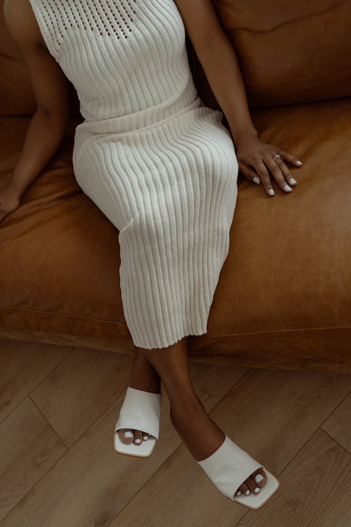 A sophisticated, minimalist portrait capturing the elegance of a mother seated on a warm-toned leather couch during a mommy and me session in a DFW studio. The photo emphasizes the mother’s graceful posture and simple attire, embodying the serene essence of motherhood in Dallas and Fort Worth, Texas.